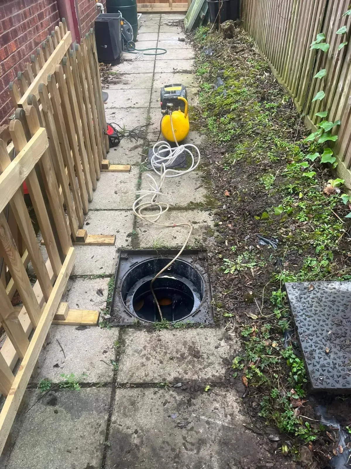 Open drain manhole with drainage equipment nearby.