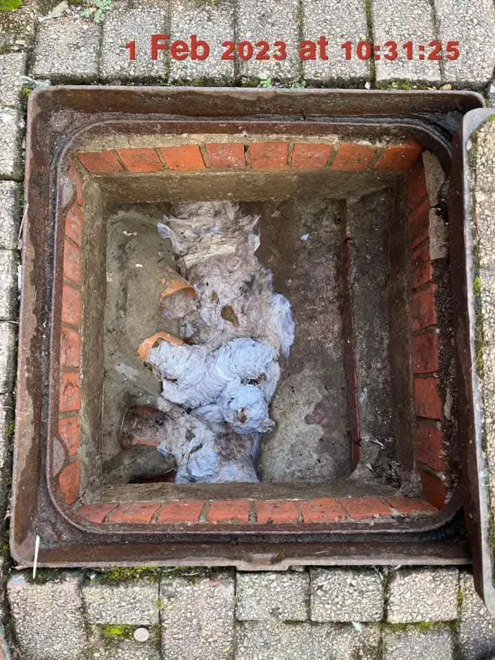 A severely blocked drain access point overflowing with wet wipes and sewage debris.