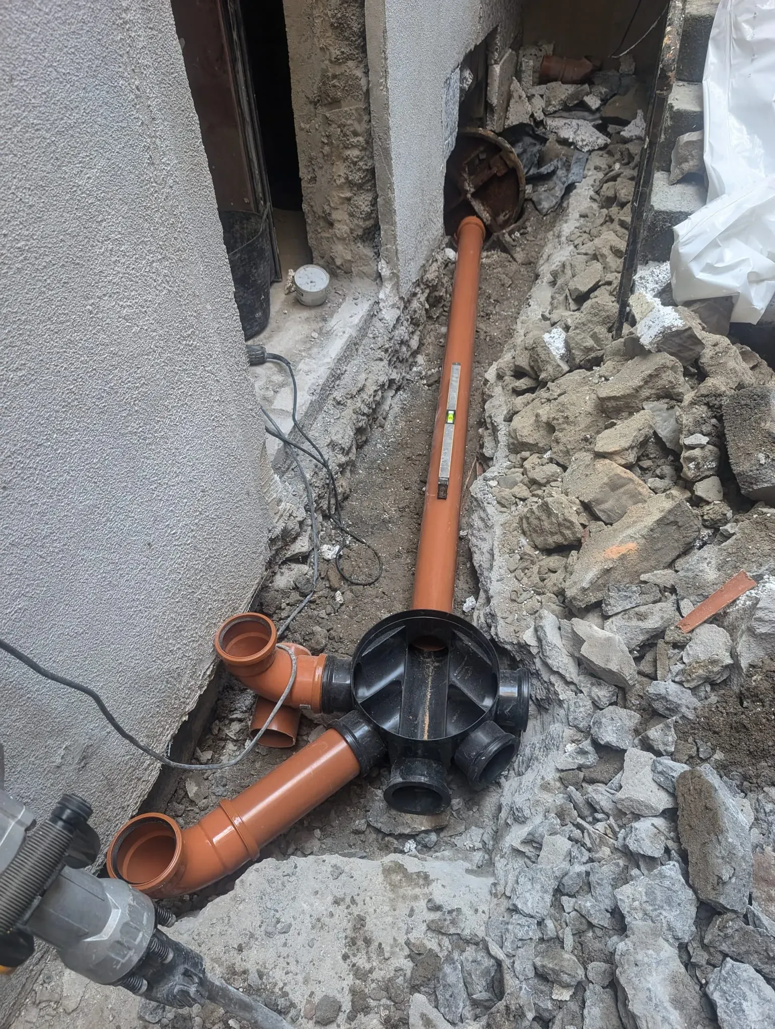 New drainage pipes and junction box being installed in an excavated trench.